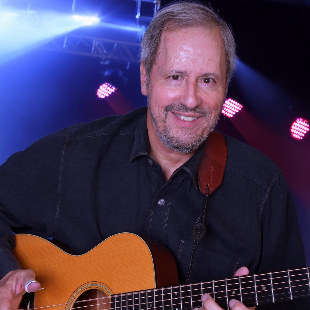 Joe Caporaso smiling with acoustic guitar under blue stage lights